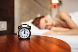 black alarm clock measuring intermittent fasting with woman getting good sleep in the background