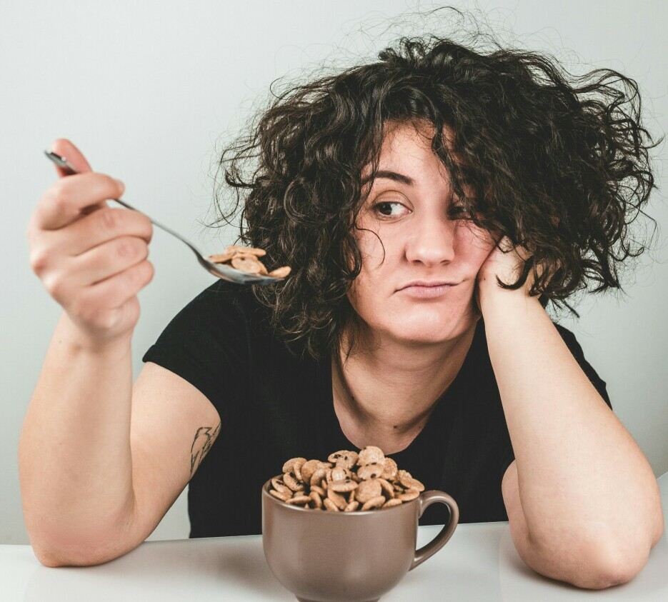 woman looking at a spoonful fo cookies with a contemplating expression